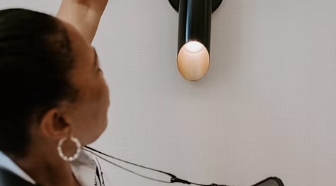 A person reaching up to adjust or inspect a modern black tubular wall sconce.