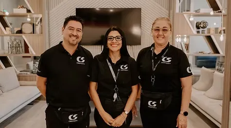 Three smiling cleaning staff members wearing matching black CleanSpace uniforms standing together in a modern lounge.