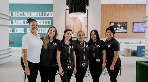 Six smiling female cleaning staff members in uniforms posing together in a modern lobby.