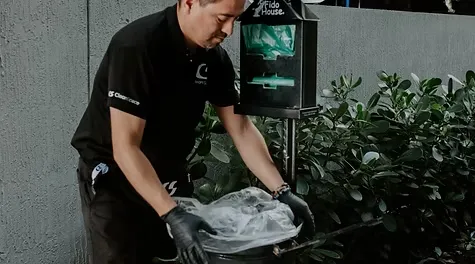 A male cleaner in a black uniform changing the trash liner at a pet waste station.