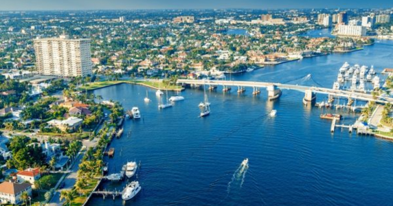Aerial view of a coastal city waterway featuring boats, a drawbridge, marina, and surrounding residential buildings.