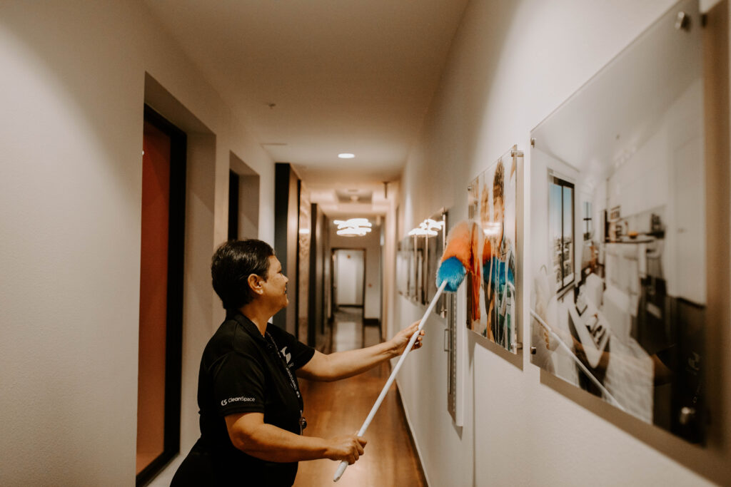 Clean Space cleaner dusting wall artwork in a Florida building hallway