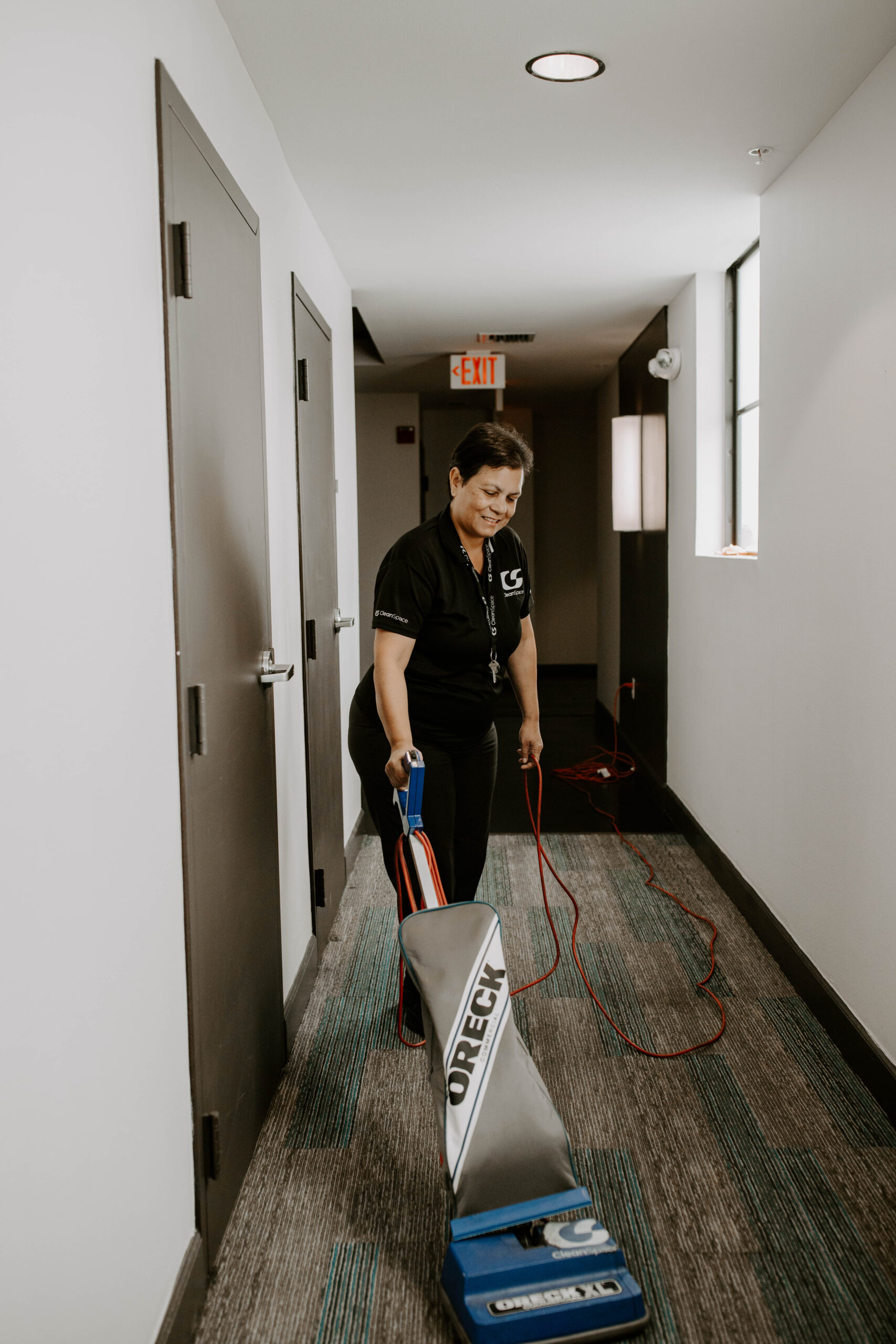 Clean Space cleaner vacuuming a carpeted hallway in a Florida apartment building